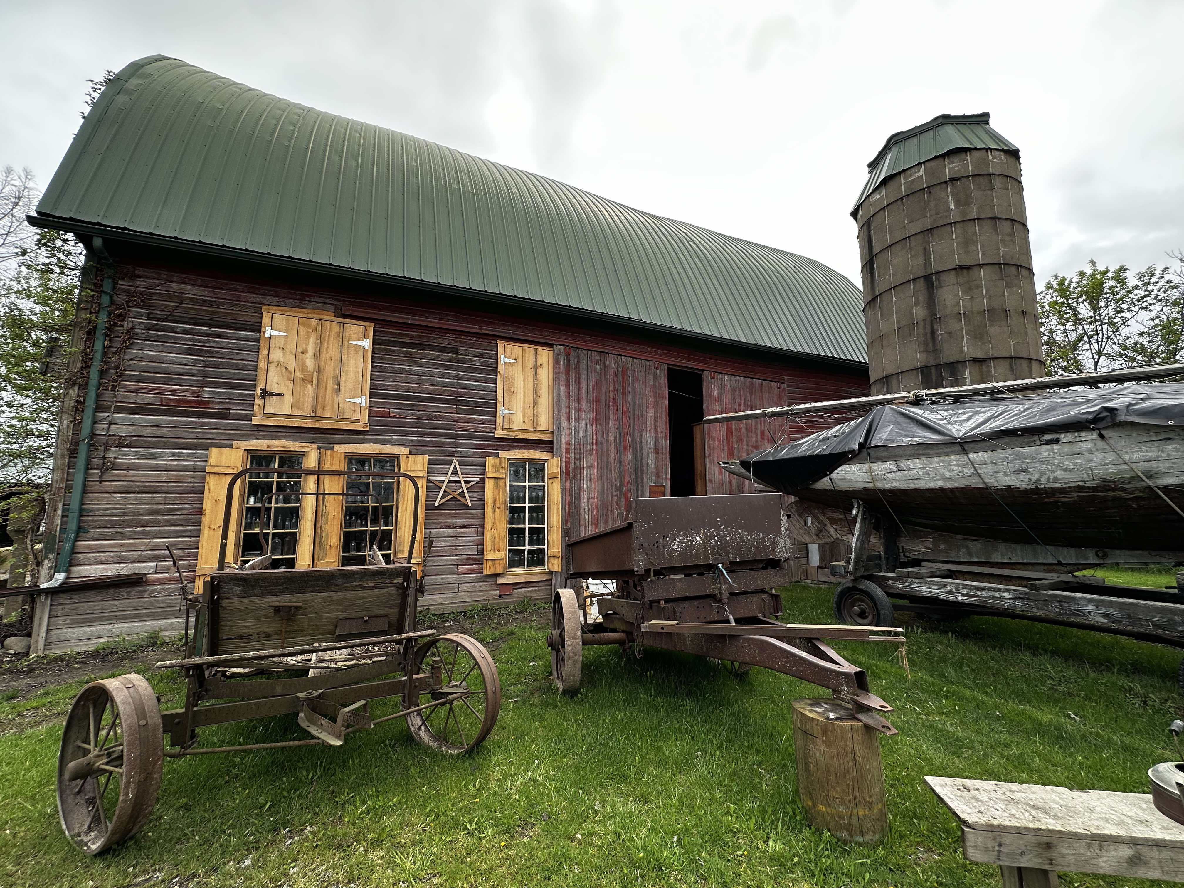  A barn with a wooden sailing ship infront of it along with a Ford Model A dump bed and a menure spreader